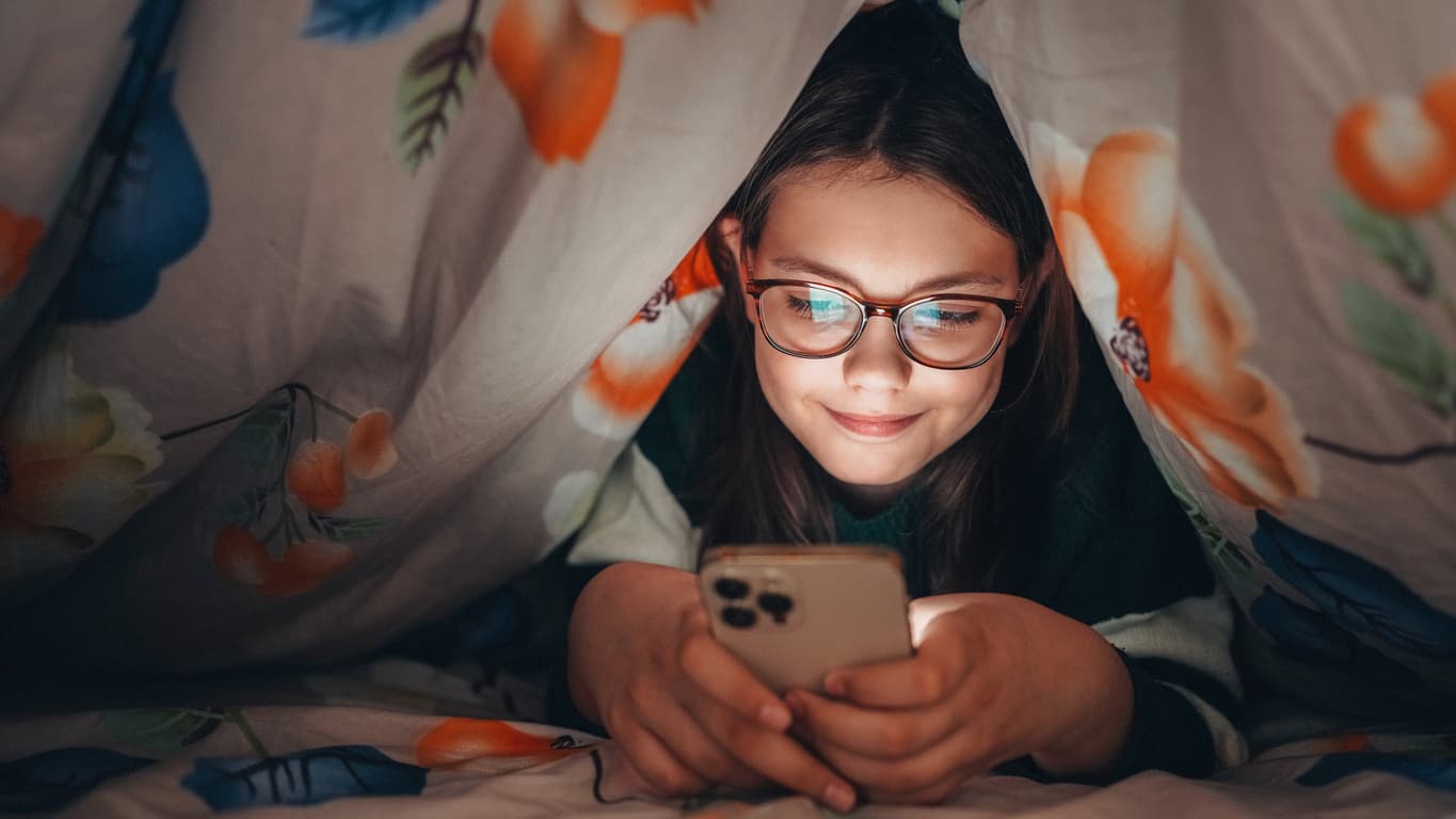a kid under covers looking at phone